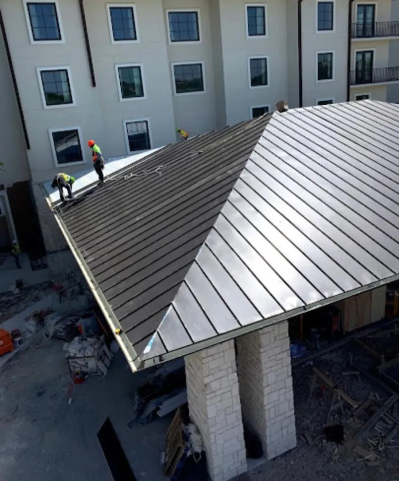 Crew installing standing seam metal roof panels on a commercial project in Tontitown